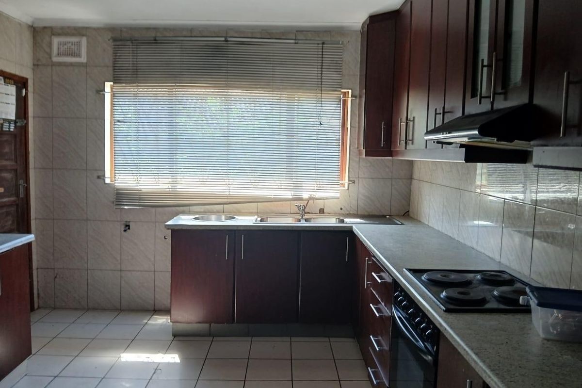 A functional kitchen featuring dark wood cabinetry, built-in oven with electric hob, extractor fan, and tiled finishes throughout.