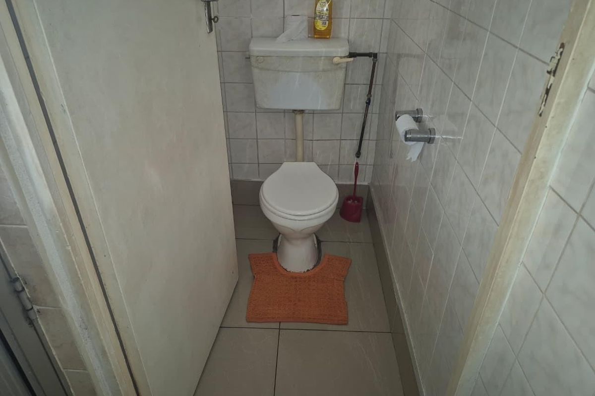 A compact, tiled guest bathroom featuring a standard toilet and basic fixtures, currently in need of cosmetic updates.