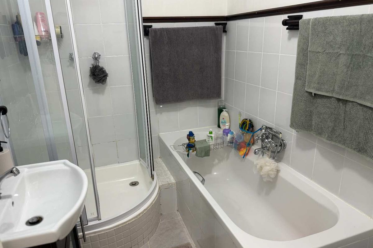 A functional bathroom featuring a white bathtub, a separate corner shower enclosure, and a pedestal sink with tiled walls.