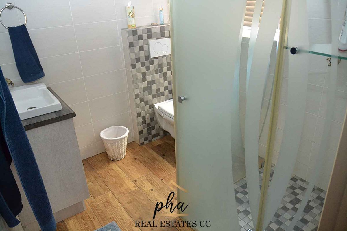 Modern bathroom featuring a wall-mounted toilet, vanity with basin, and a glass-enclosed shower with mosaic tile accents.