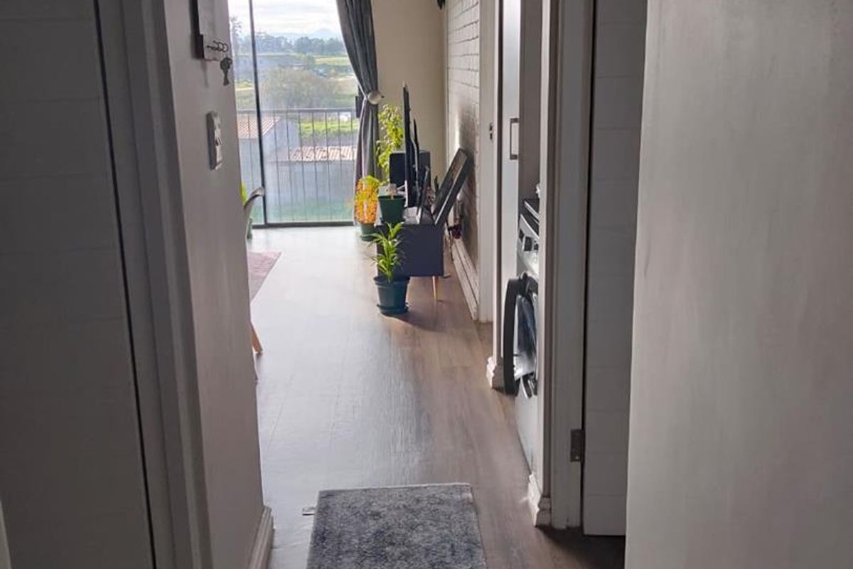 A bright hallway featuring laminate flooring and an exposed brick wall, leading towards a sliding glass door with access to an outdoor balcony.