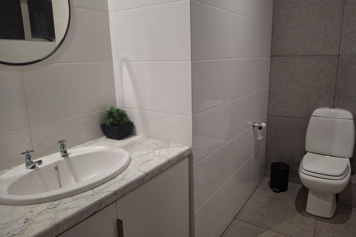 Modern bathroom featuring a marble-topped vanity cabinet, white wall tiling, and a contemporary toilet with grey floor and accent wall tiles.