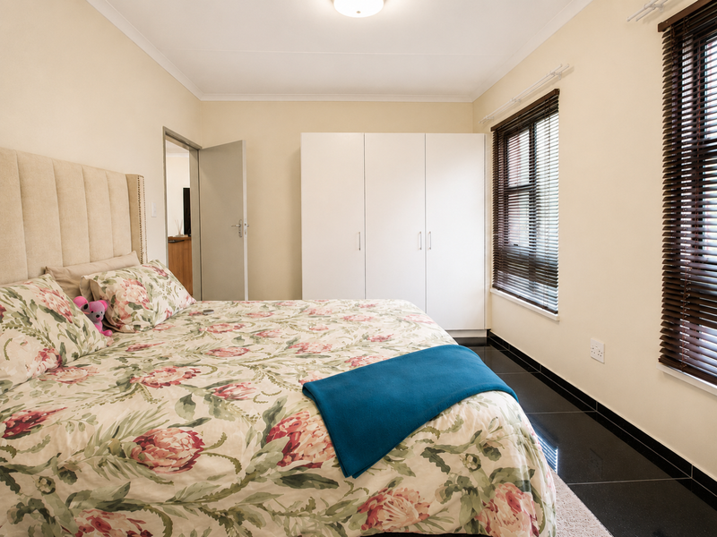 A well-maintained bedroom featuring built-in cupboards, dark tiled flooring, and venetian blinds, offering a clean and functional living space.