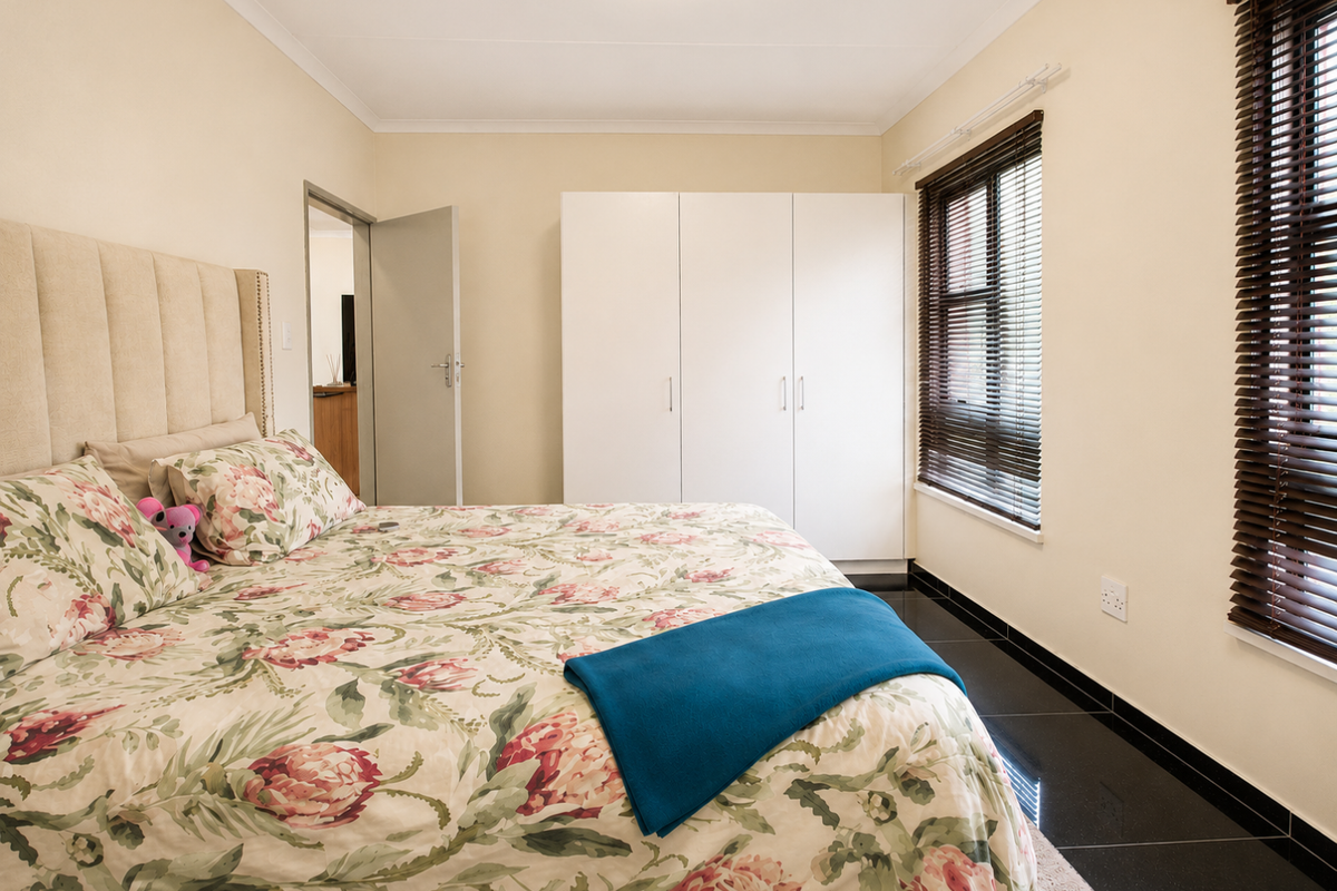 A well-maintained bedroom featuring built-in cupboards, dark tiled flooring, and venetian blinds, offering a clean and functional living space.