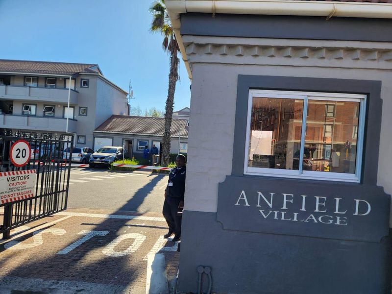 The entrance to Anfield Village apartment complex, featuring a security gatehouse, boom gate access, and paved driveway.