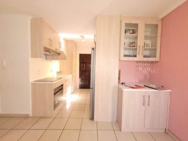 A functional kitchen featuring light wood-finish cabinetry, integrated appliances including a hob and oven, and tiled flooring throughout.