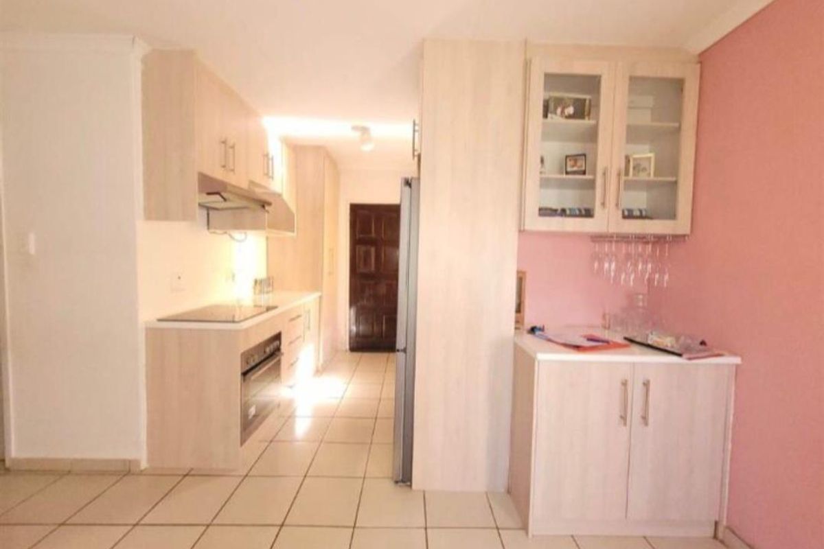 A functional kitchen featuring light wood-finish cabinetry, integrated appliances including a hob and oven, and tiled flooring throughout.