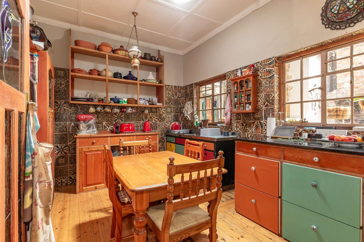 A rustic kitchen featuring timber cabinetry, patterned tiled splashbacks, wooden flooring, and built-in shelving, offering a warm and traditional aesthetic.