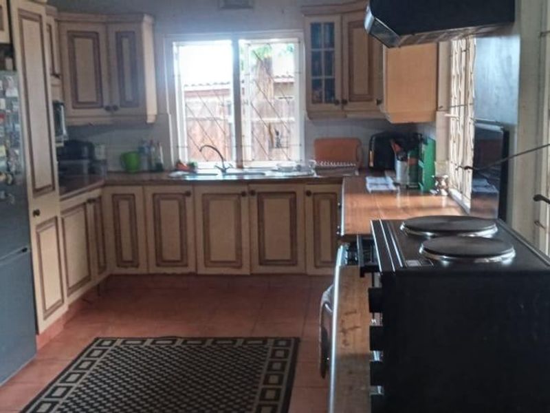 A functional kitchen featuring wooden cabinetry, a double sink, and tiled flooring, with a security gate providing access to the exterior.