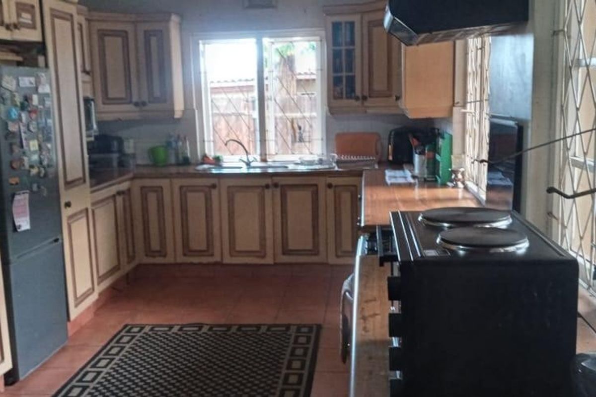 A functional kitchen featuring wooden cabinetry, a double sink, and tiled flooring, with a security gate providing access to the exterior.