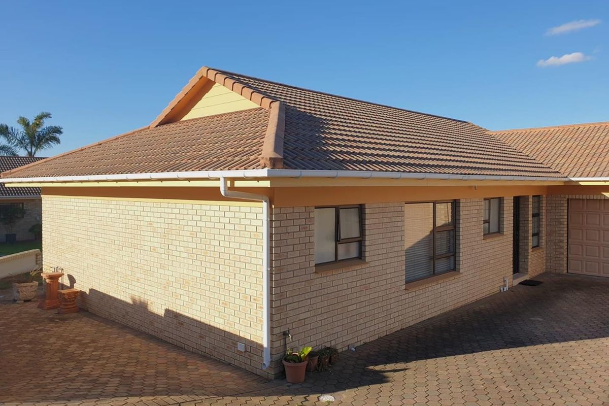 A view of the side and rear exterior of a brick house featuring a tiled roof, guttering, and paved driveway area.