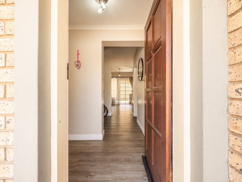 A bright entrance hallway featuring laminate flooring and a classic timber panelled front door, leading through to the main living area.