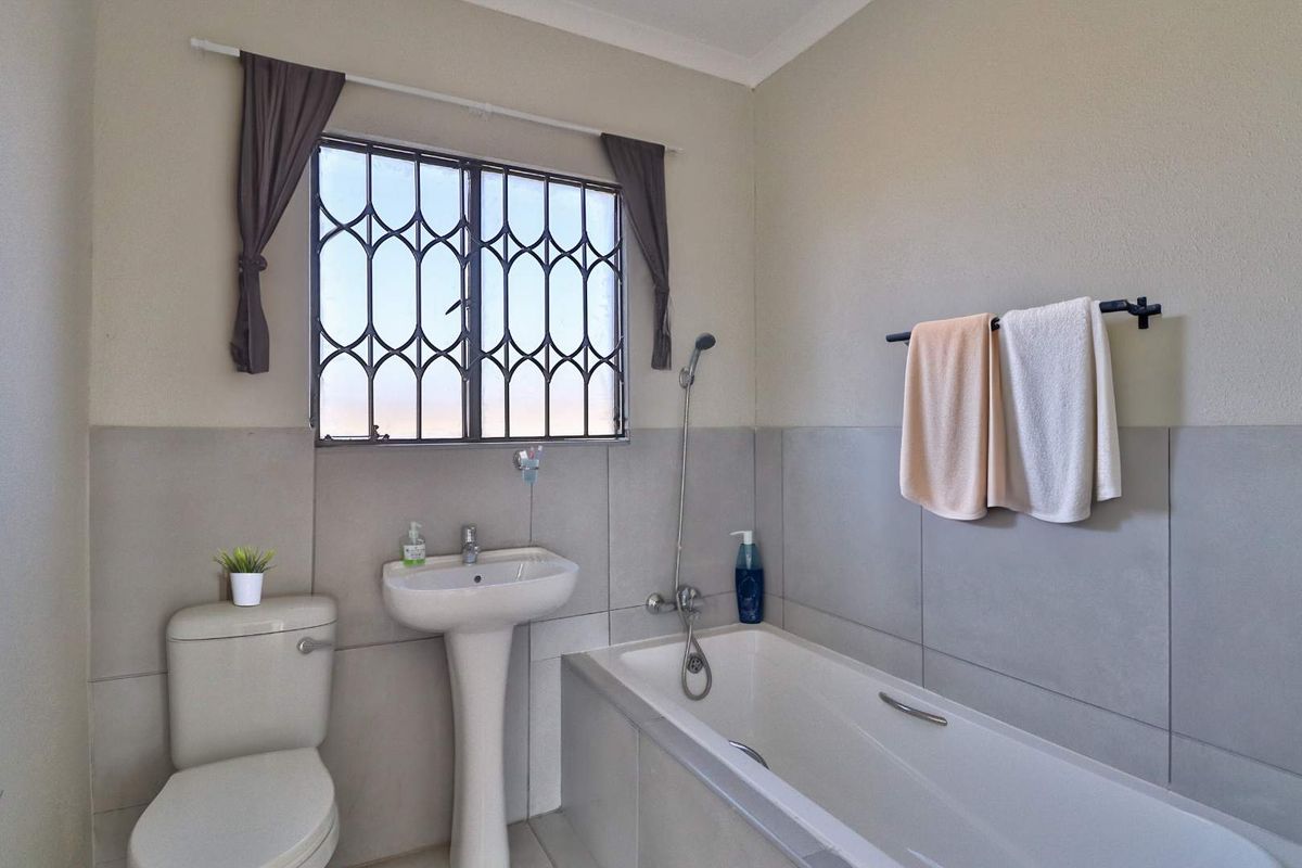 A functional bathroom featuring a pedestal basin, a bathtub with a handheld shower attachment, and a toilet, finished with neutral wall tiling.