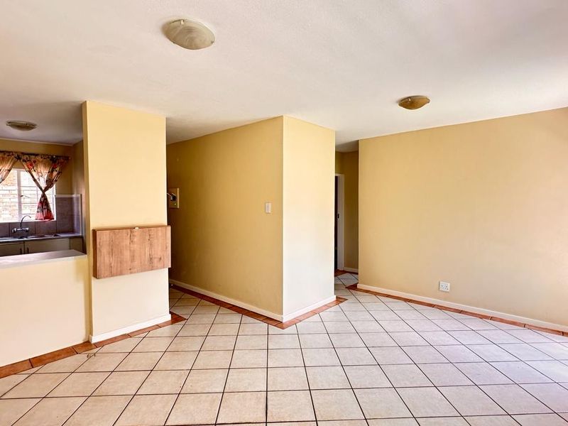 An open-plan living and kitchen area featuring tiled flooring, neutral walls, and functional built-in cabinetry, offering a blank canvas for modern interior design.