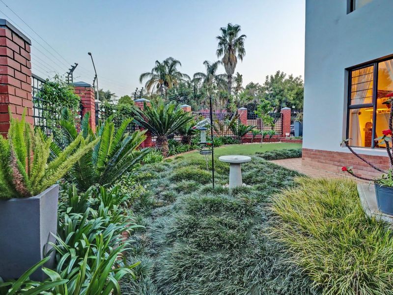 A well-maintained garden featuring a paved walkway, lush landscaping, and secure brick boundary walls with electric fencing.