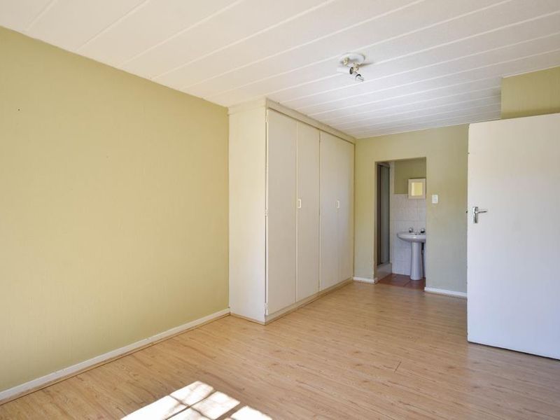 An empty bedroom featuring laminate flooring, built-in cupboards, and direct access to an en-suite bathroom with a pedestal basin.