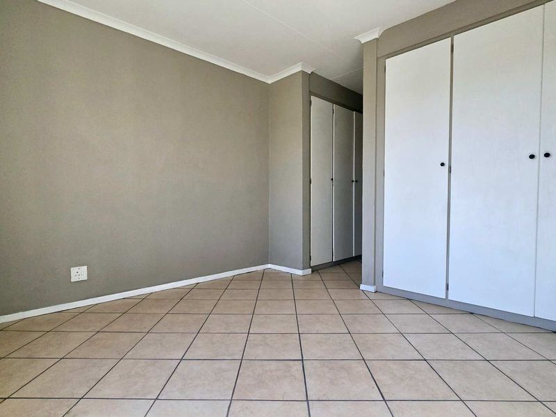 An empty bedroom featuring neutral wall paint, tiled flooring, and built-in storage cupboards.