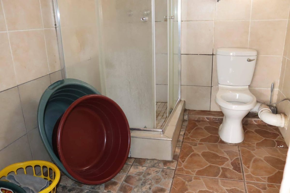 A functional bathroom featuring a corner shower enclosure and a standard toilet with tiled flooring and wall finishes.