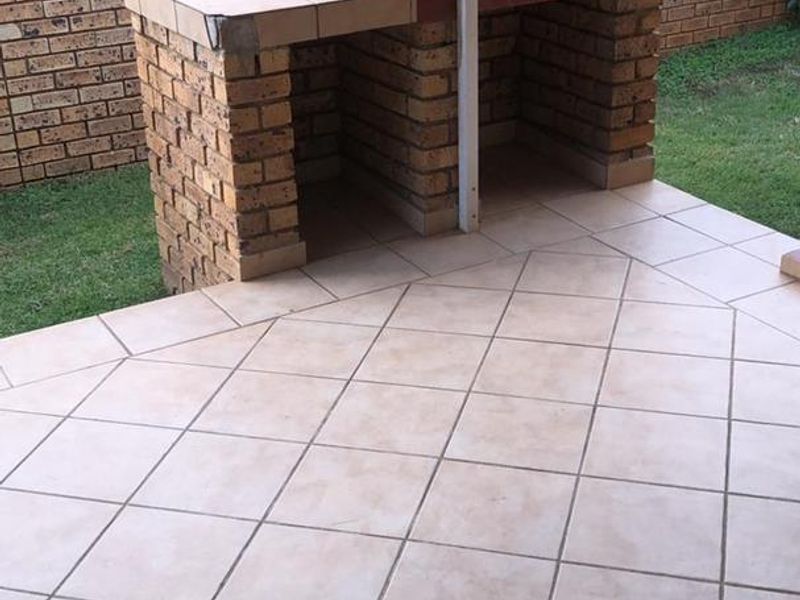 Outdoor patio area featuring a built-in brick braai, tiled flooring, and a private garden space enclosed by brick boundary walls.