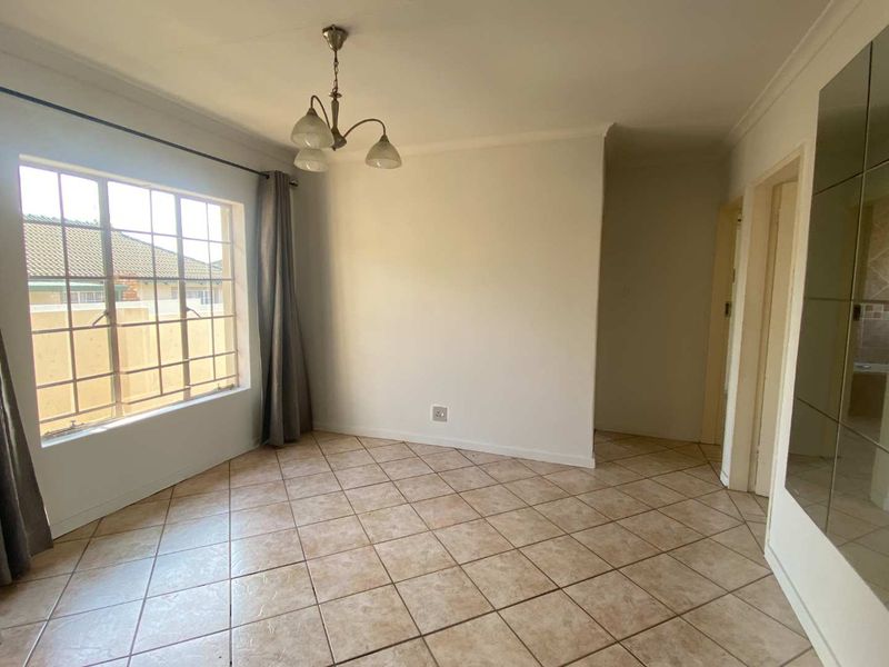 A bright, empty living area featuring neutral tiled flooring, a decorative ceiling light, and a large mirrored wall panel.