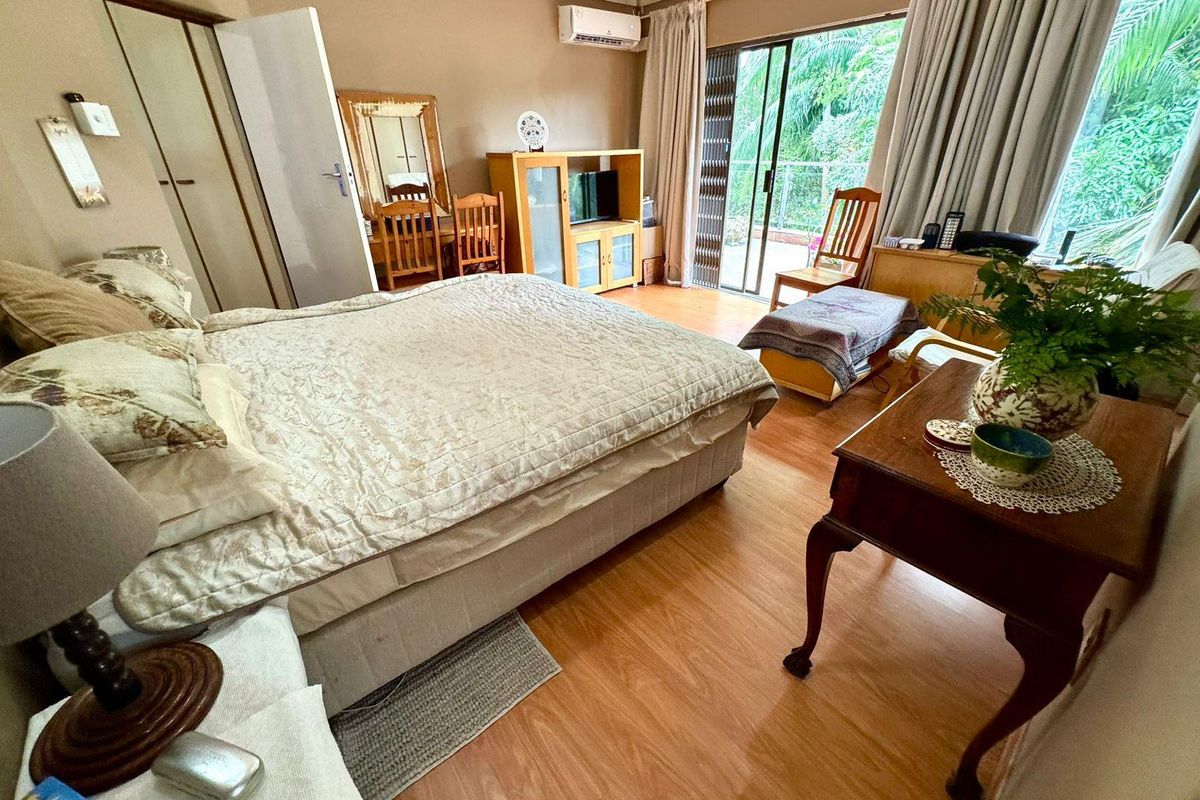 Spacious bedroom featuring wood-look flooring, built-in cupboards, wall-mounted air conditioning unit, and sliding glass doors leading to an outdoor balcony area.