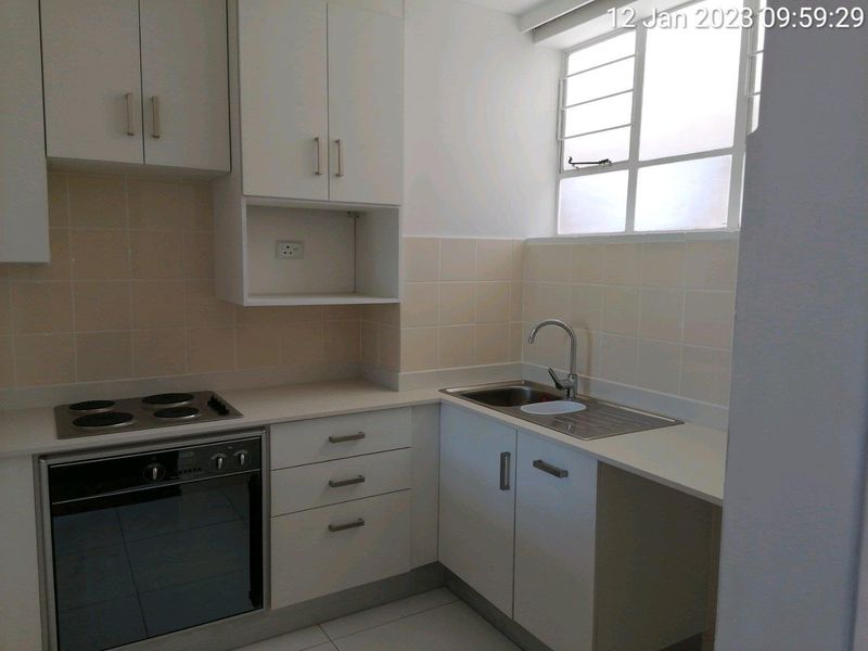 A clean, functional kitchen featuring white built-in cabinetry, a stainless steel sink, an electric hob, and an integrated oven with tiled splashback.