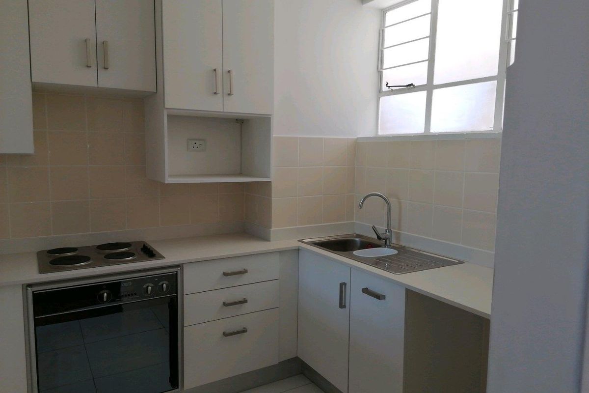 A clean, functional kitchen featuring white built-in cabinetry, a stainless steel sink, an electric hob, and an integrated oven with tiled splashback.