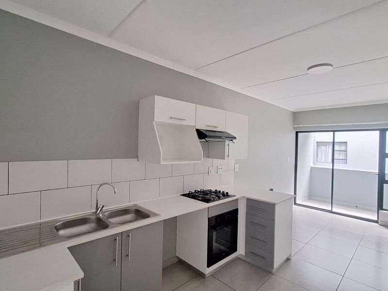 Modern open-plan kitchen featuring sleek cabinetry, gas hob, built-in oven, and tiled flooring, leading to a bright balcony area.