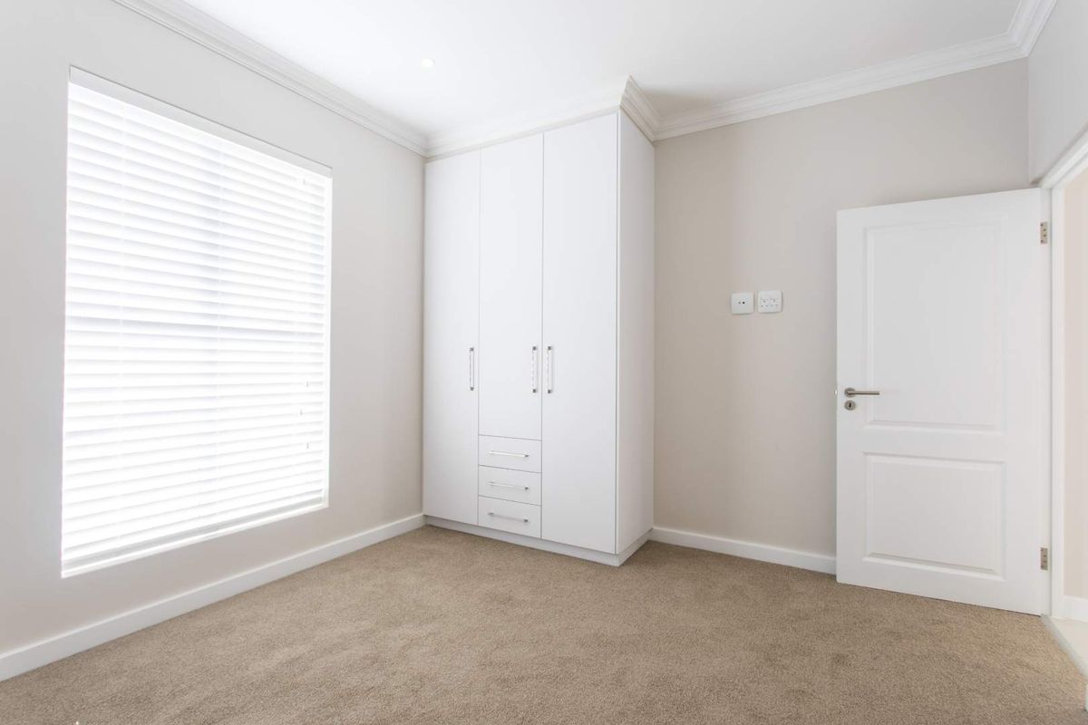 A bright, neutral bedroom featuring plush carpeting, built-in white cabinetry, and clean architectural finishes, offering a versatile space ready for personalization.