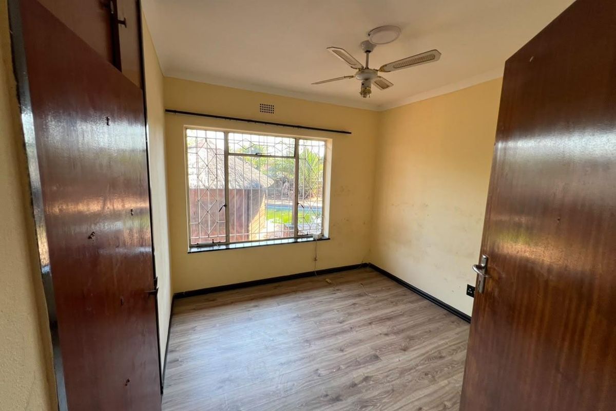 An empty bedroom featuring laminate flooring, built-in cupboards, a ceiling fan, and security bars on the window.