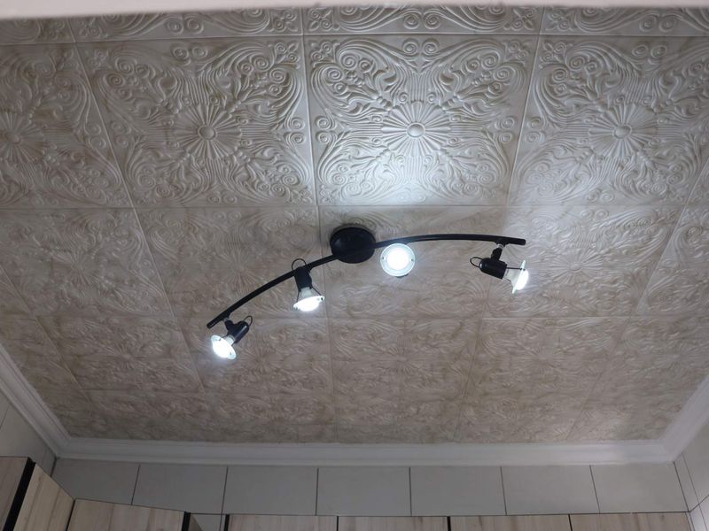 A close-up view of a ceiling featuring decorative embossed tiles, crown molding, and a modern four-light track fixture.