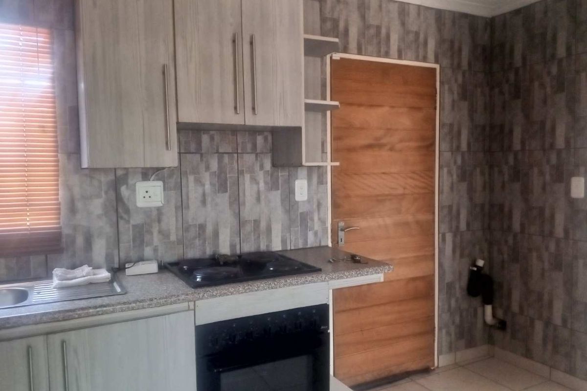A compact kitchen featuring built-in cabinetry, a built-in oven with hob, stainless steel sink, and modern grey tiled wall finishes.