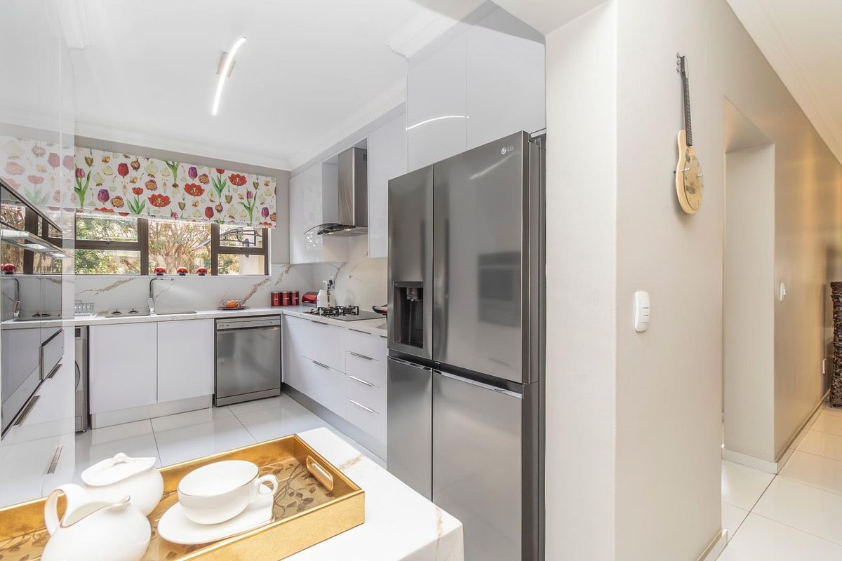 Modern kitchen featuring sleek white cabinetry, stone countertops, stainless steel appliances, and tiled flooring, offering a clean and functional culinary space.