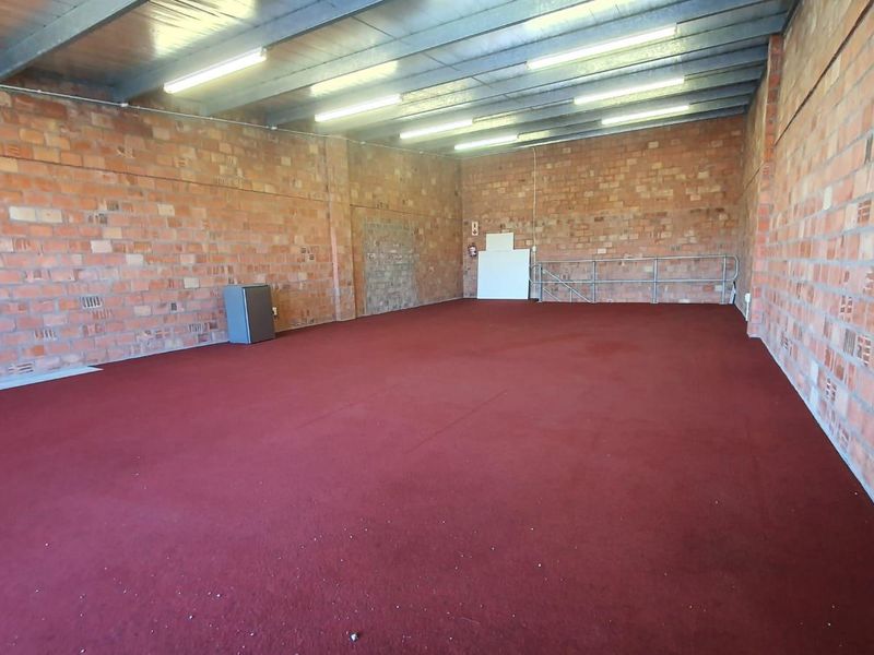 A large, open-plan utility or storage space featuring exposed brick walls, industrial steel ceiling beams, and red carpet flooring.