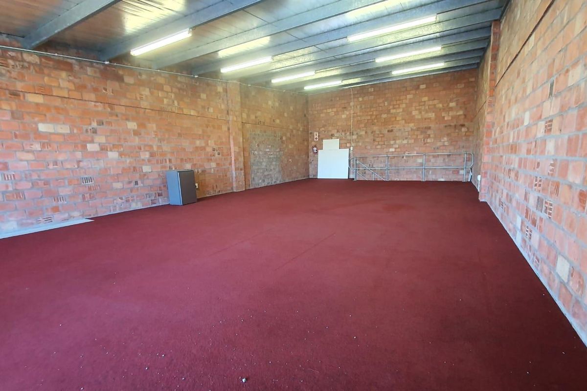 A large, open-plan utility or storage space featuring exposed brick walls, industrial steel ceiling beams, and red carpet flooring.