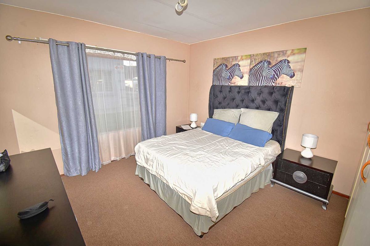 A standard bedroom featuring neutral wall tones, carpeted flooring, and a large window with curtain tracks.