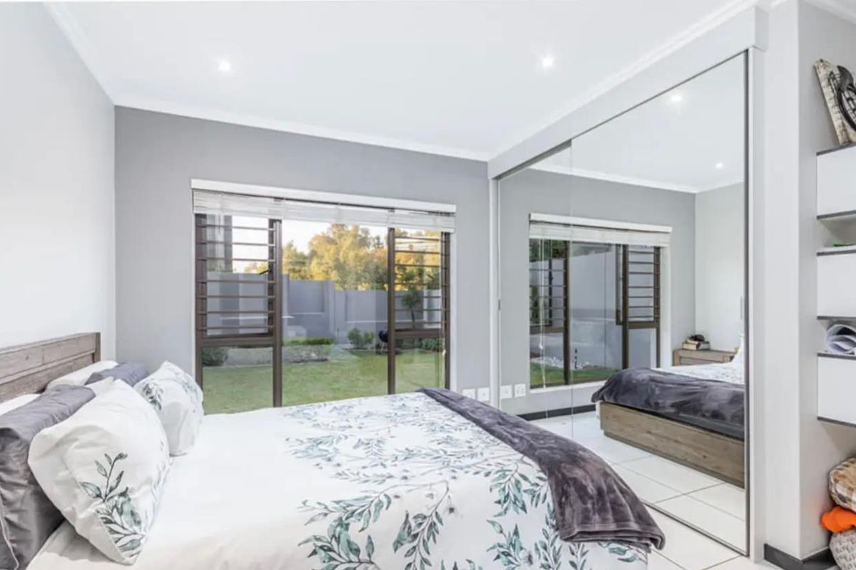 A bright bedroom featuring tiled floors, recessed lighting, and a large built-in mirrored wardrobe with direct access to the garden through sliding glass doors.