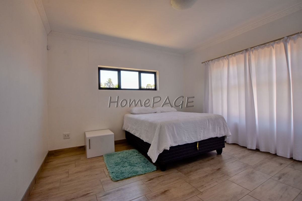 A bright bedroom featuring modern tiled flooring, decorative cornicing, and large windows with curtain tracks.
