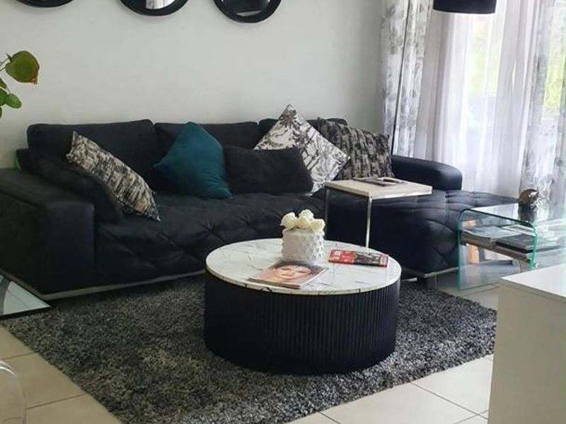 A well-maintained living room featuring neutral tiled flooring and large windows with curtain tracks, providing a bright and comfortable living space.