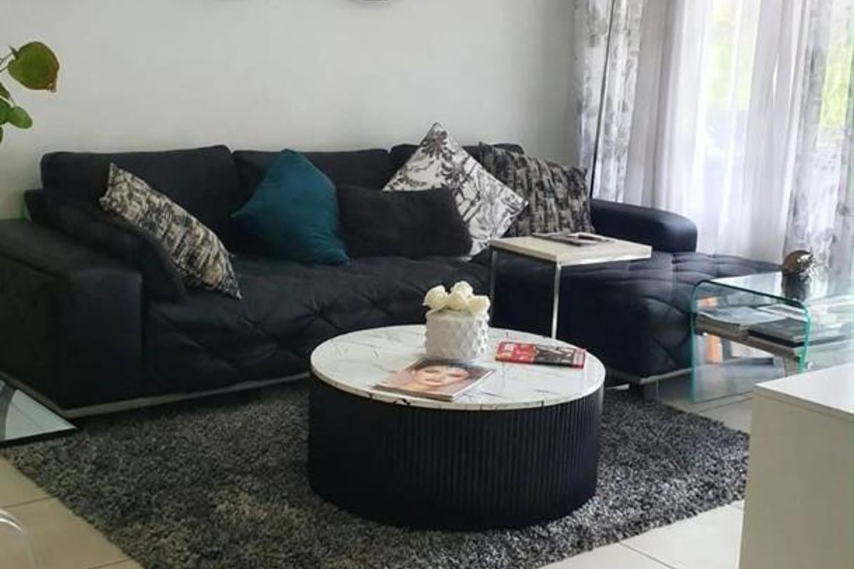 A well-maintained living room featuring neutral tiled flooring and large windows with curtain tracks, providing a bright and comfortable living space.