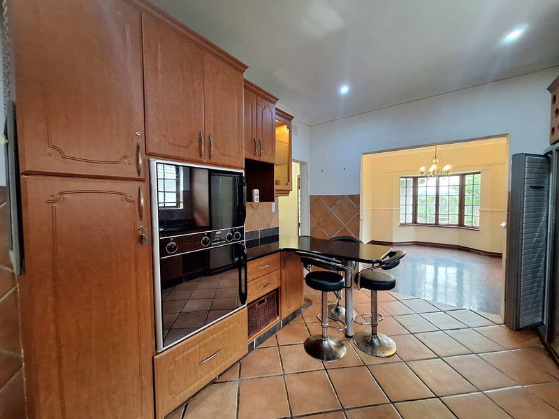 Open-plan kitchen featuring traditional timber cabinetry, built-in oven, and tiled flooring, flowing into an adjacent dining area with large bay windows.
