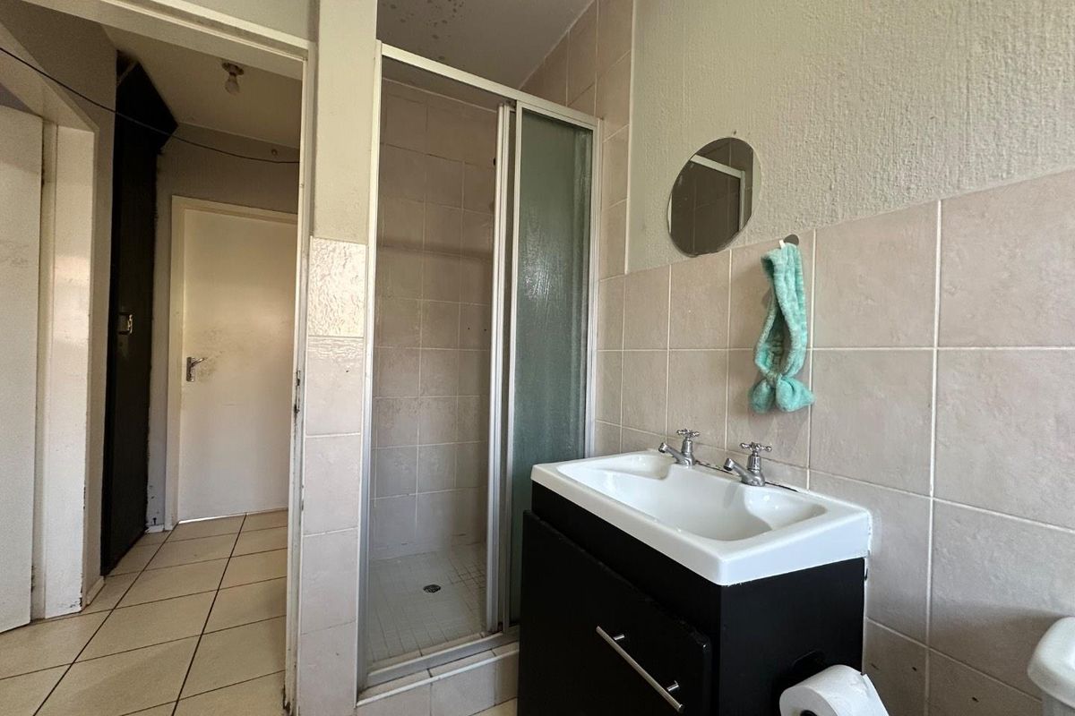 A functional bathroom featuring a shower cubicle, vanity basin, and tiled walls, requiring cosmetic updates to improve its overall condition.