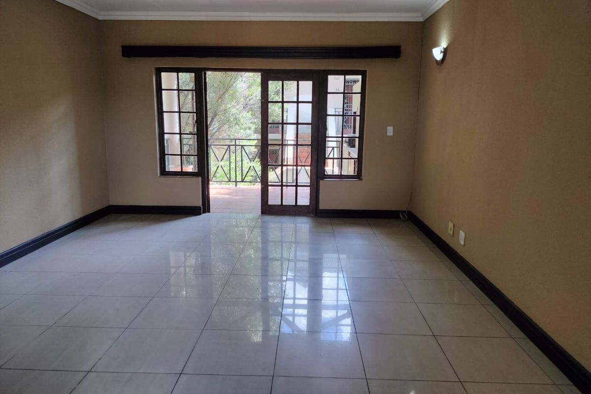 Spacious, empty living area featuring neutral walls, tiled flooring, and direct access to an outdoor balcony through a glass-paneled door.