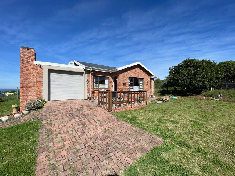 Front view of a single-story brick house featuring a paved driveway, attached garage, and a small timber deck entrance.