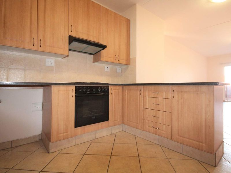 A functional kitchen featuring light wood-finish cabinetry, black granite countertops, a built-in oven with extractor fan, and tiled flooring.