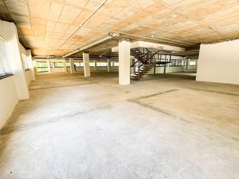 Expansive open-plan commercial office space featuring an industrial aesthetic with exposed concrete ceilings, ducting, and a central metal staircase.