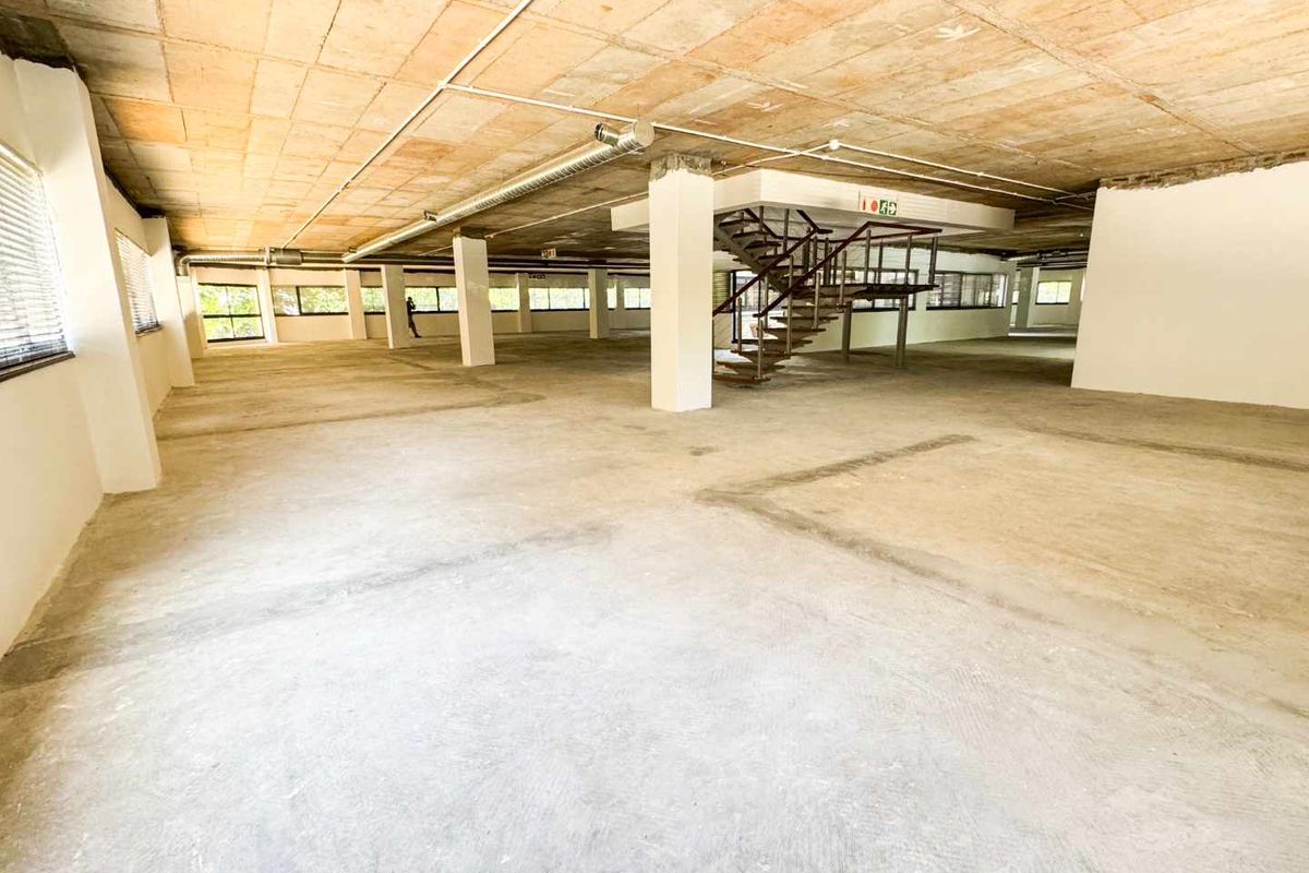 Expansive open-plan commercial office space featuring an industrial aesthetic with exposed concrete ceilings, ducting, and a central metal staircase.