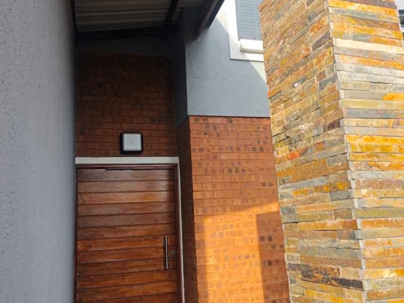 Modern entrance featuring a timber front door, exposed brickwork, and a striking stone-clad pillar under a covered porch area.