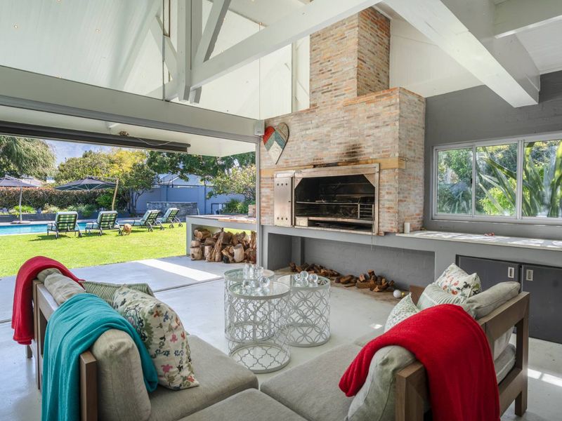 Spacious covered patio featuring a large built-in brick fireplace, exposed timber rafters, and seamless flow to the garden and pool area.