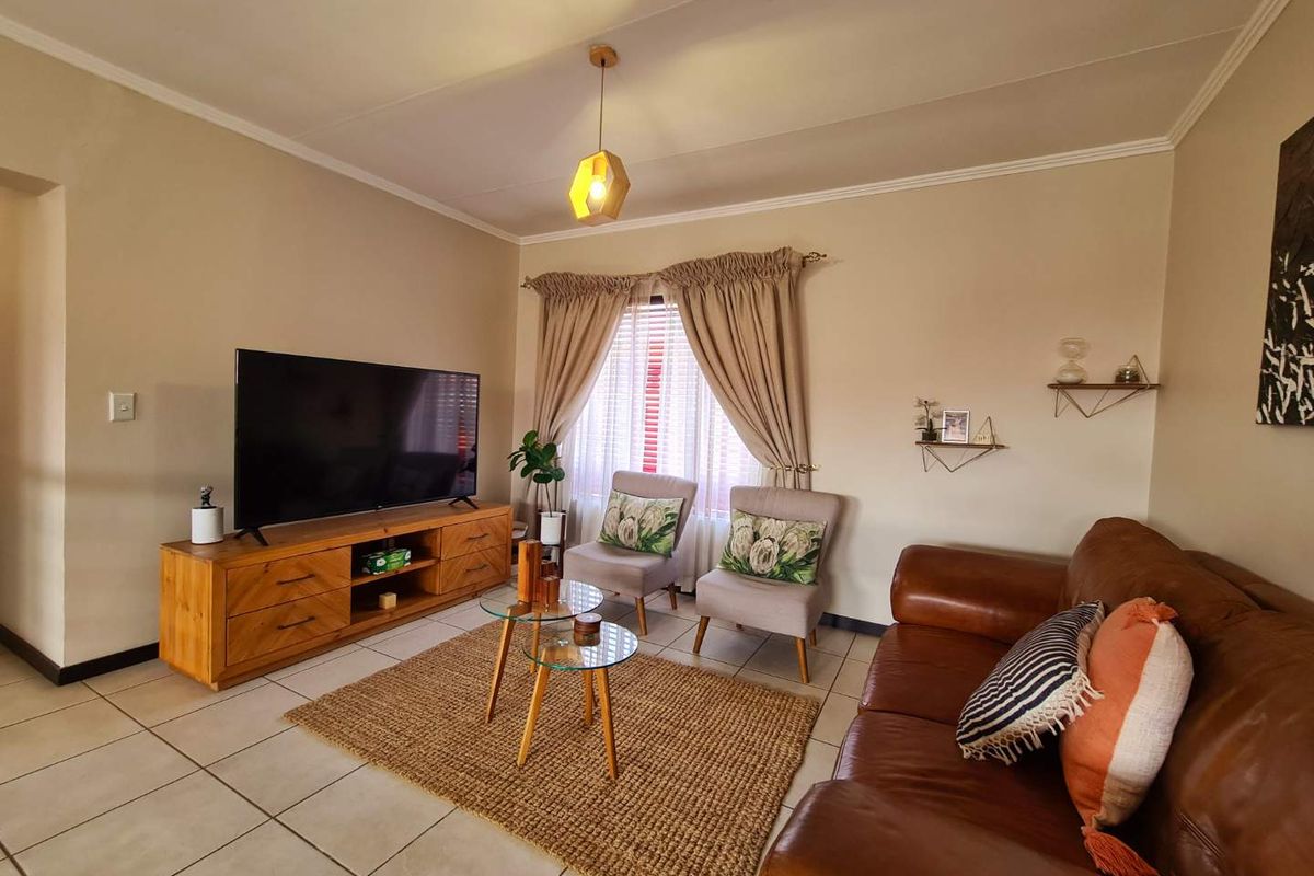 A comfortable living room featuring tiled flooring, neutral wall tones, and a large window with curtain treatments, providing a functional and inviting space.